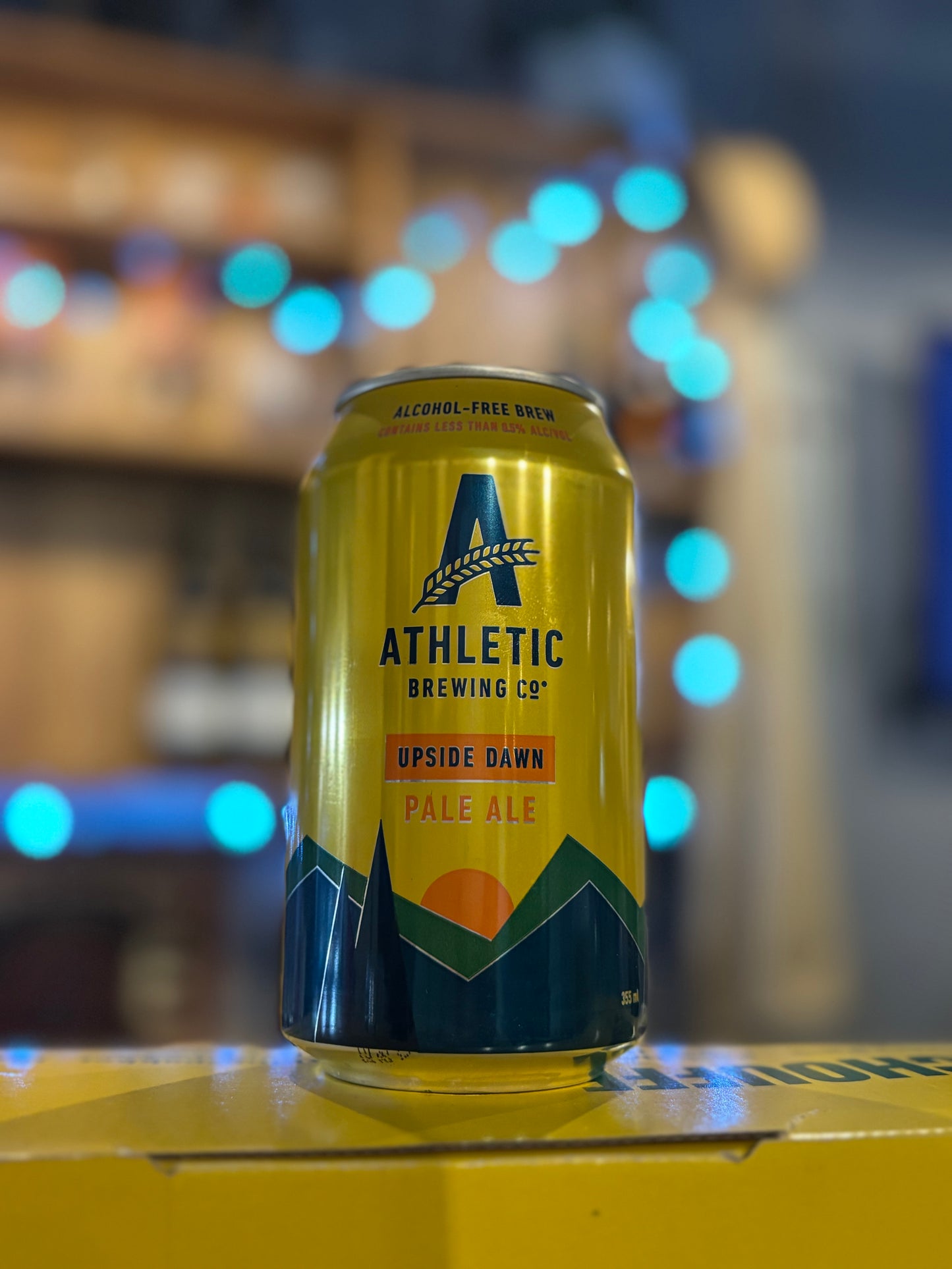 Yellow can of Athletic Brewing Co. Pale Ale on a blurred bar background