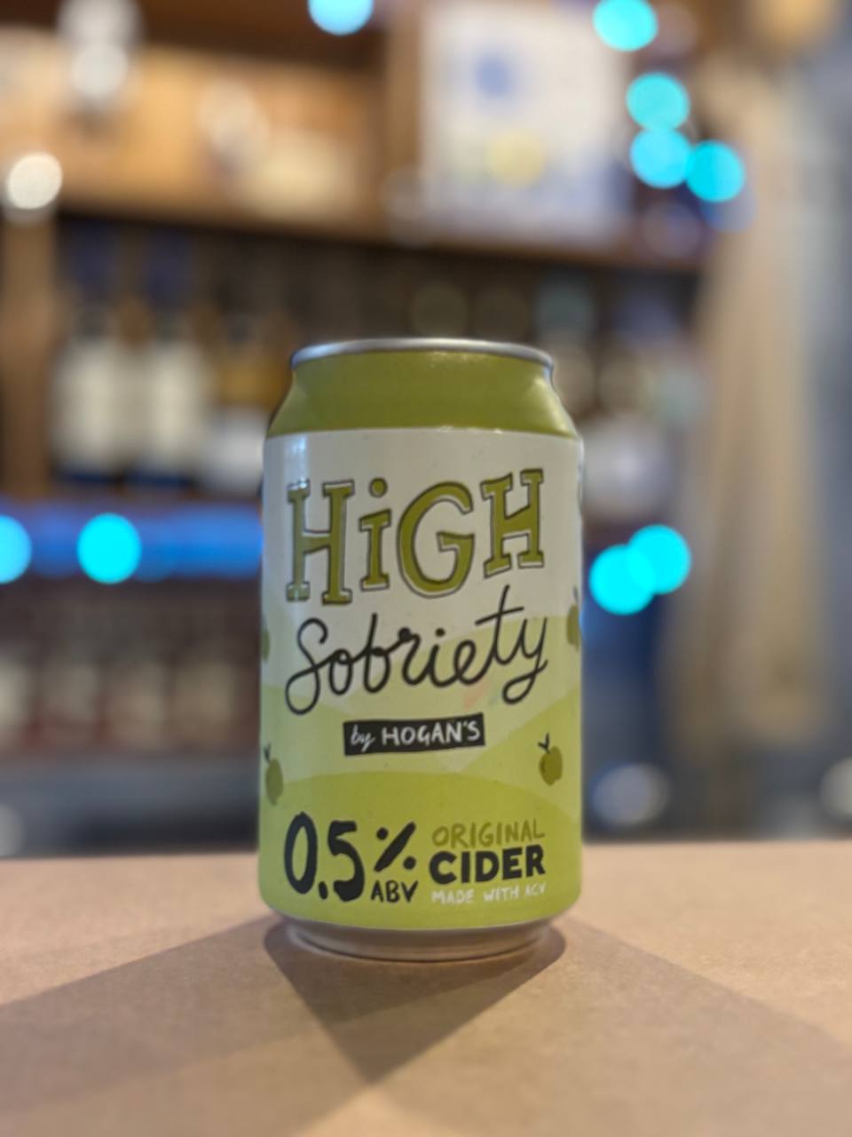 Can of 'High Sobriety' cider by Hogan's on a bar counter with a blurred bar background.