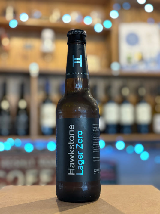 Hawkstone Lager Zero bottle on a bar counter with blurred shelves in the background