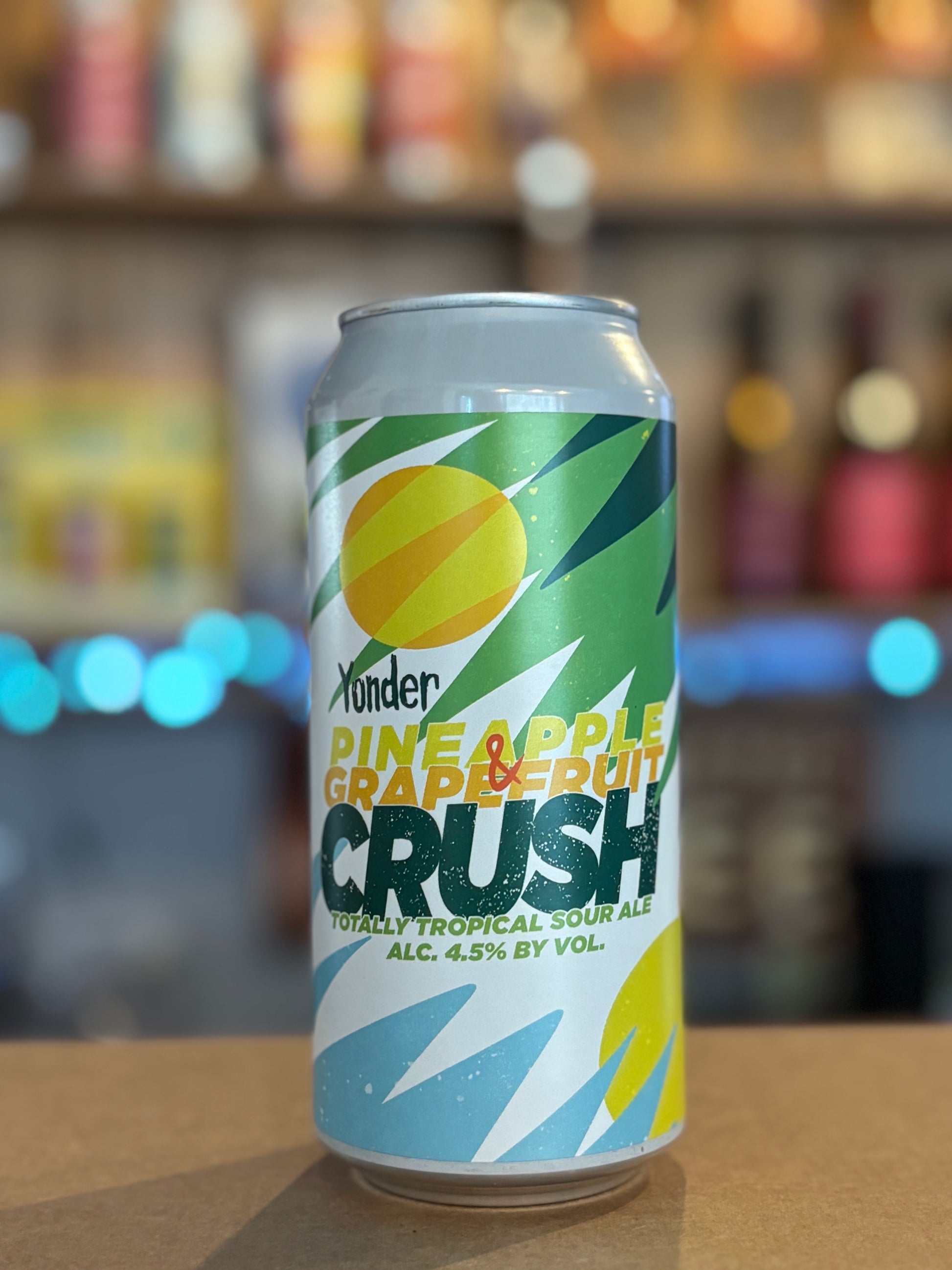 Can of Pineapple Grapefruit Crush beer on a bar counter with blurred shelves in the background
