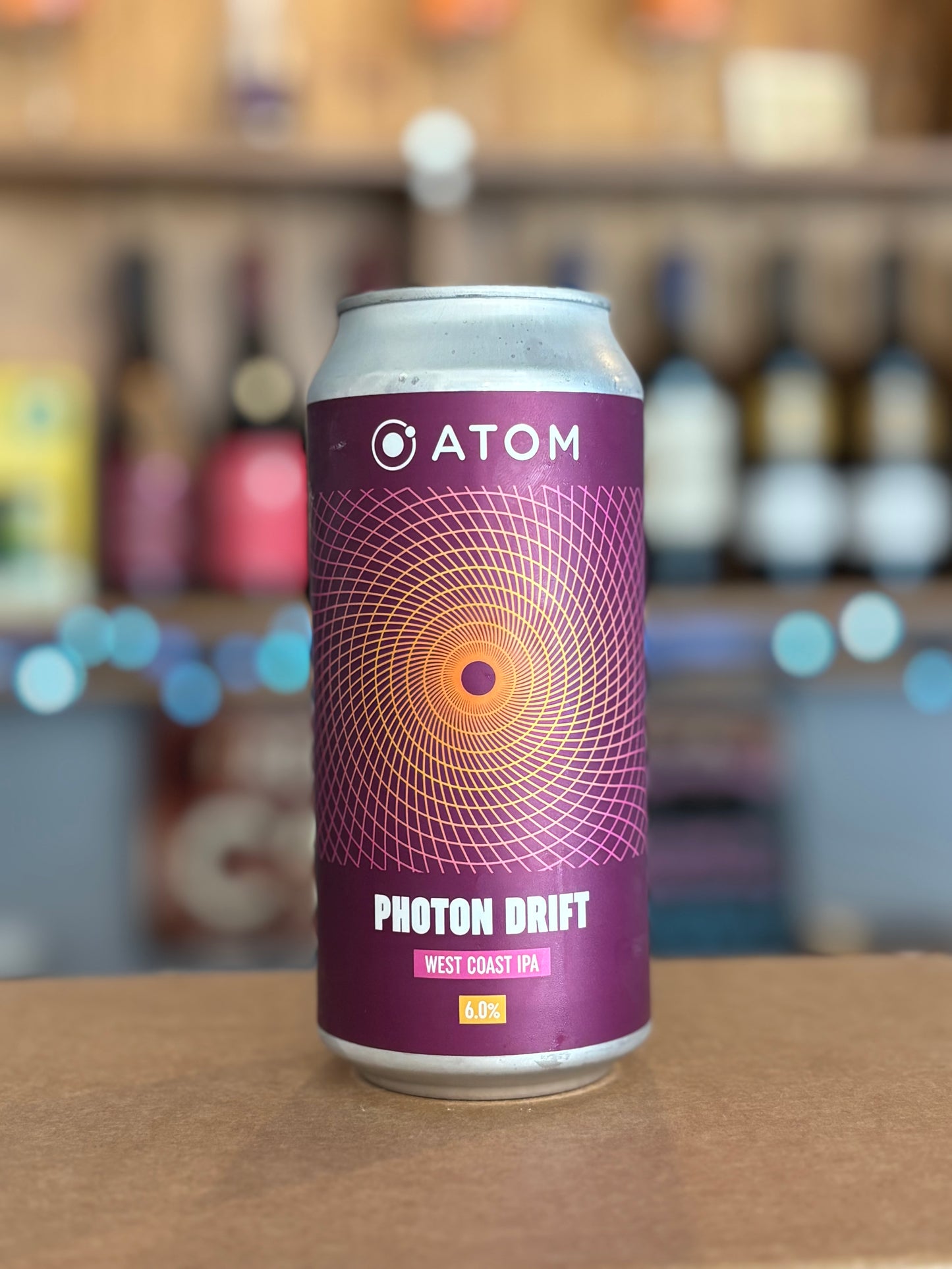 Purple can of Atom Photon Drift beer on a bar counter with blurred bottles in the background