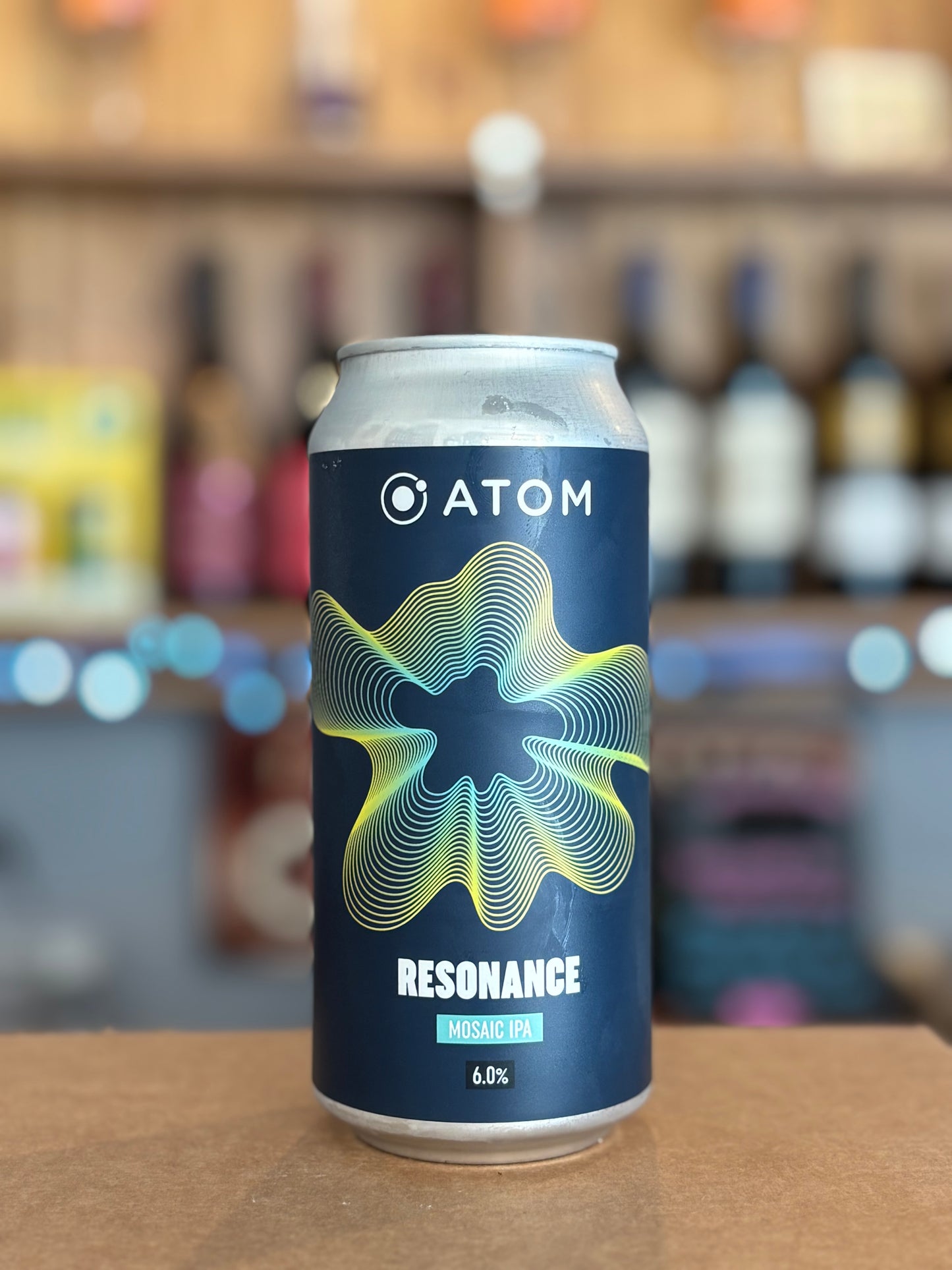 Can of Atom Resonance beer on a wooden surface with blurred bottles in the background